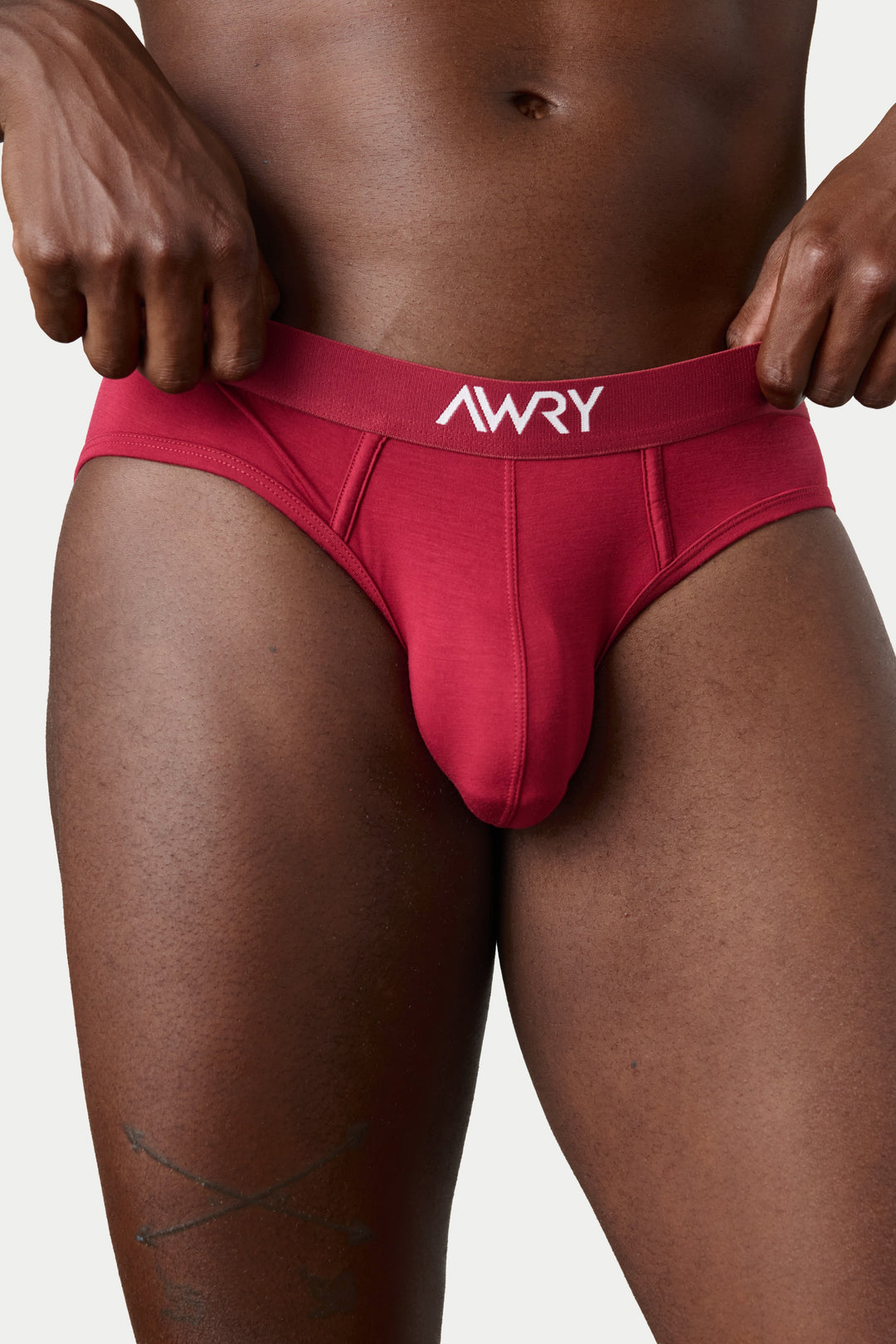 A close-up of a male model wearing a bright red jockstrap with a white &
