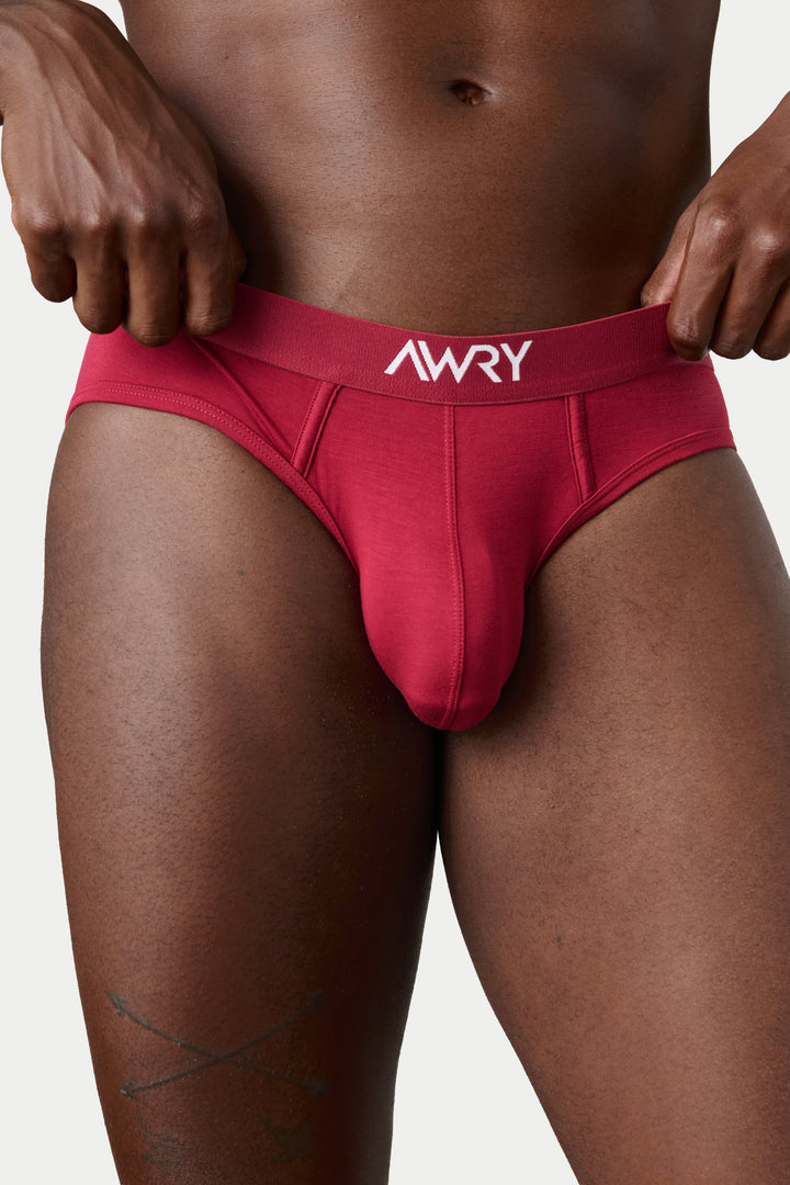 A close-up of a male model wearing a bright red jockstrap with a white &