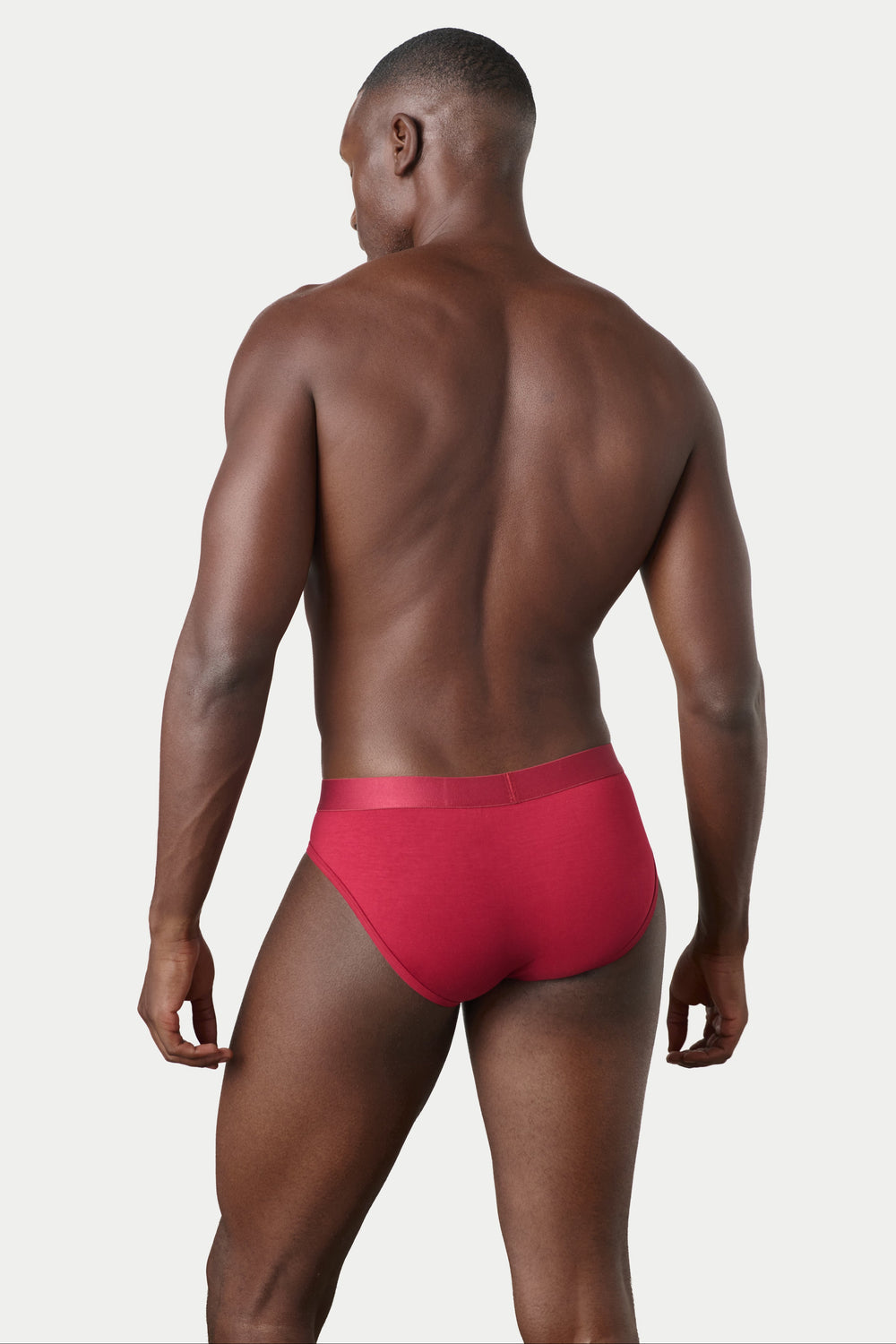 A man shown from the back wearing bright red men's briefs against a light gray studio background.