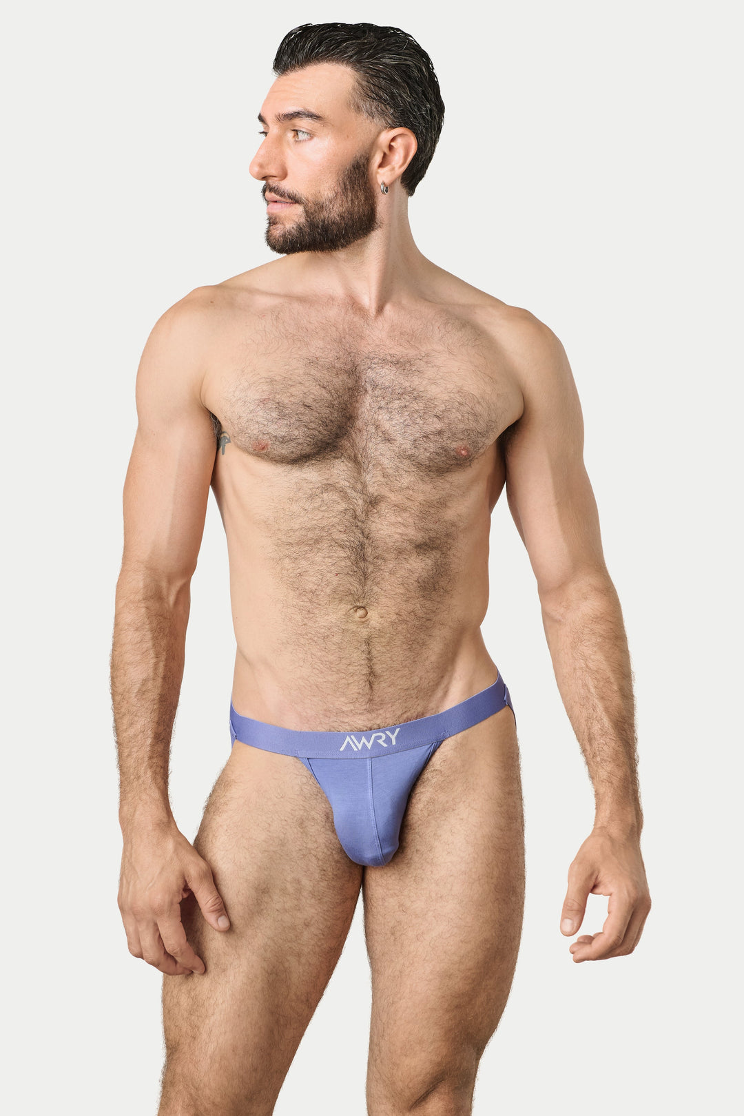 A shirtless man modeling a light purple jockstrap with the brand name 'AWRY' printed on the front, set against a plain light gray background.