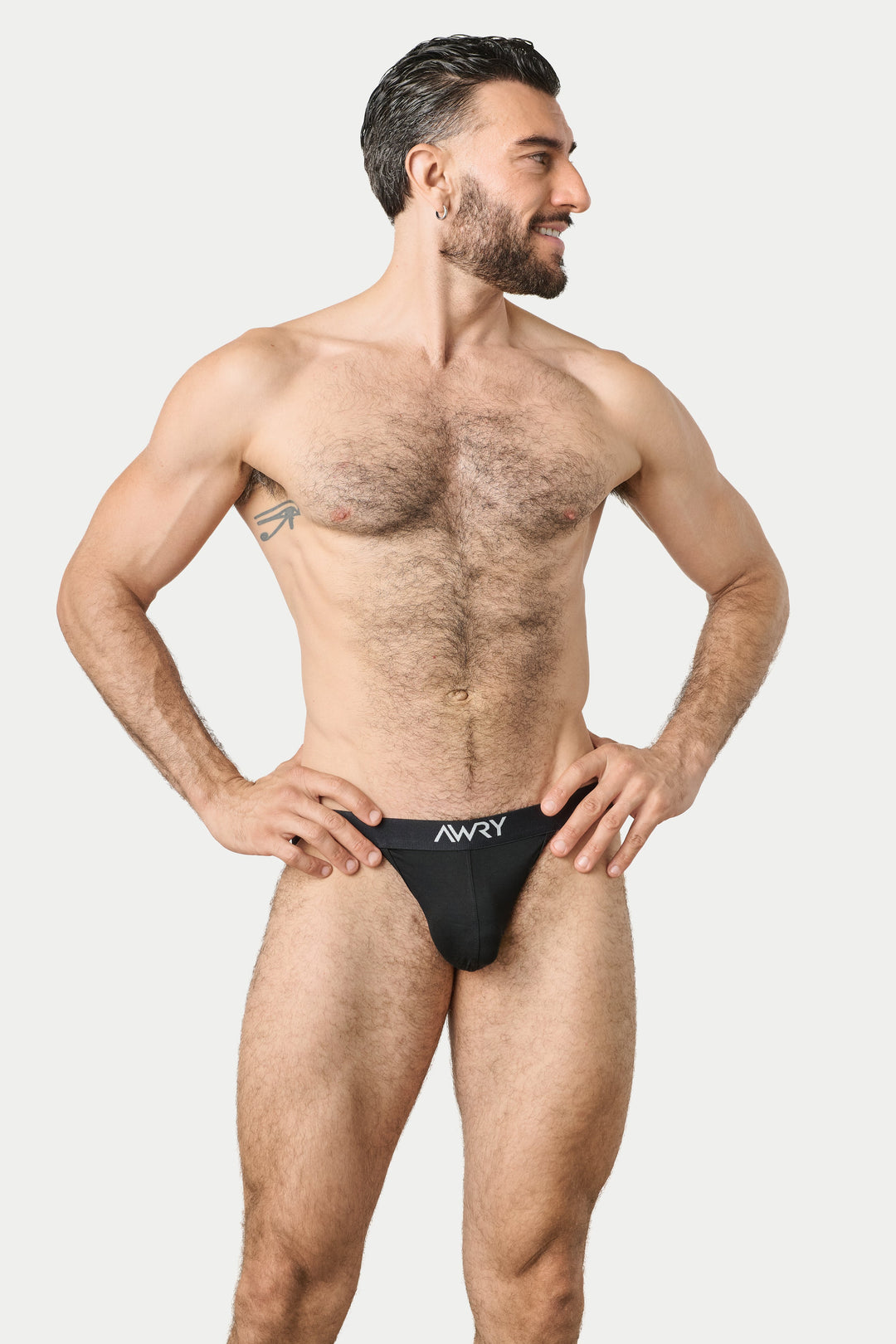 A muscular man modeling black men's briefs with a white 'AWRY' logo on the front, posed against a solid light gray background.