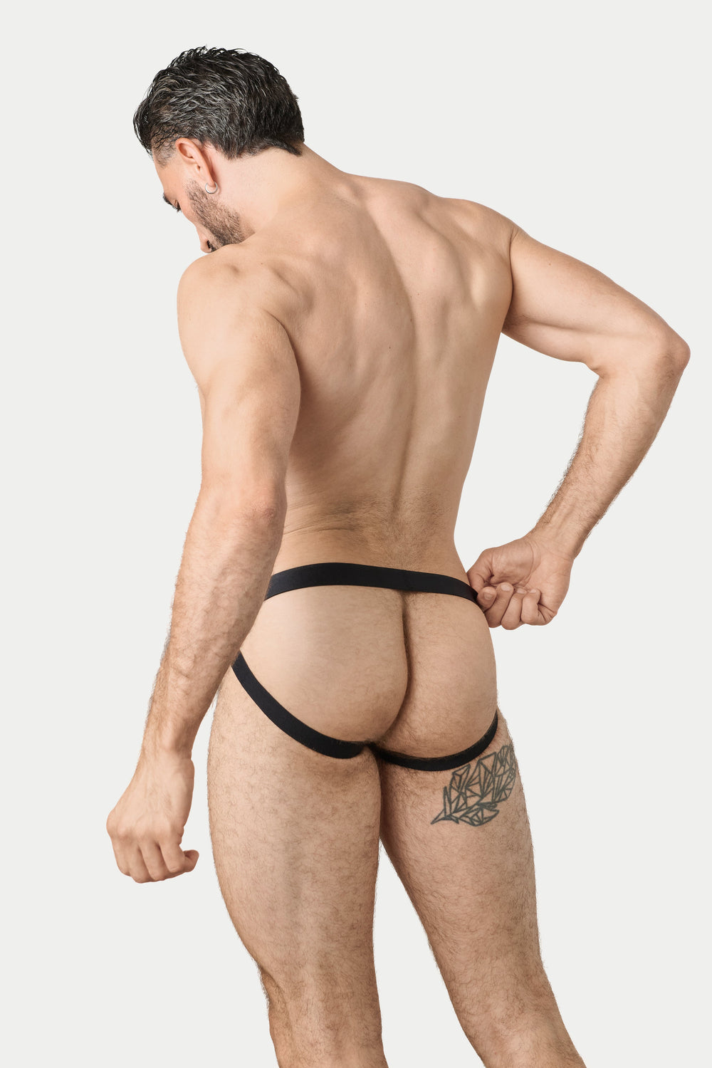 A muscular man shown from behind wearing black thong-style underwear, posing against a light gray studio background.