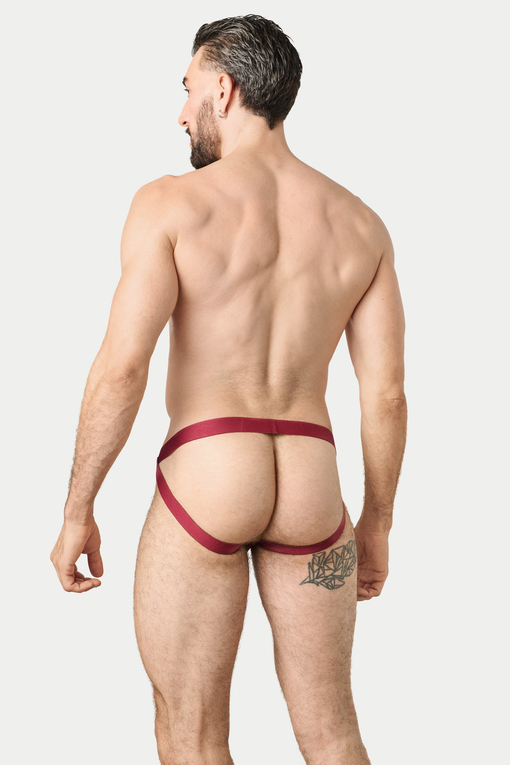 A man shown from the back wearing a jockstrap in a deep burgundy red, against a solid light gray background.