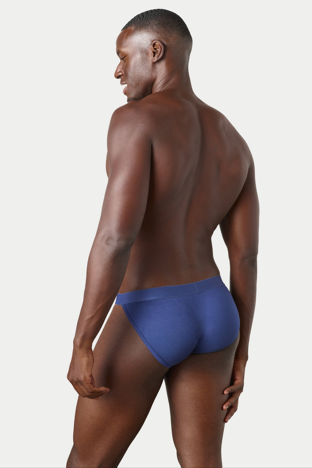 A man shown from the back wearing a pair of blue briefs, photographed against a clean light gray studio background.