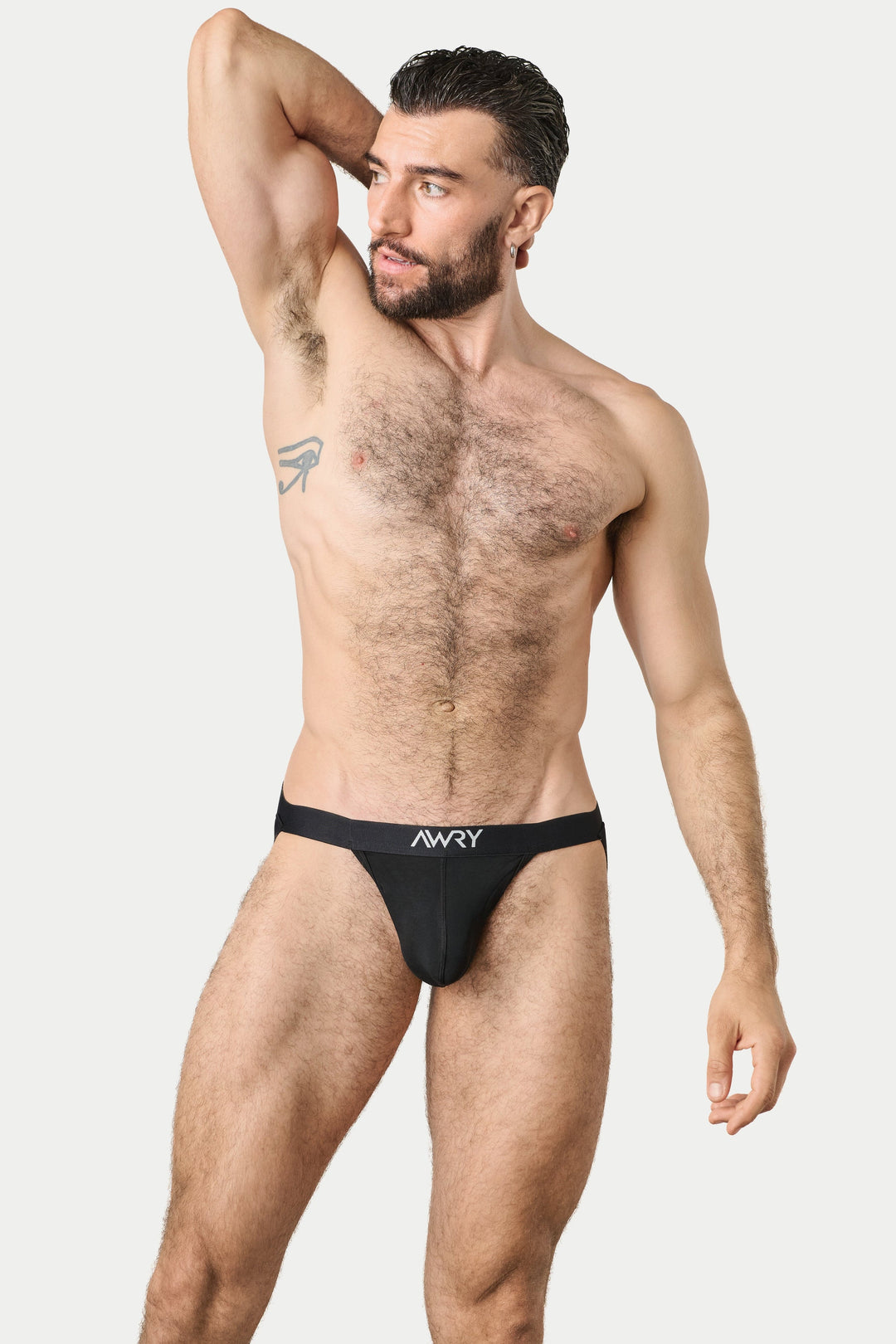 A shirtless male model wearing a black jockstrap with a white 'AWRY' logo on the front, posing against a light gray studio background.