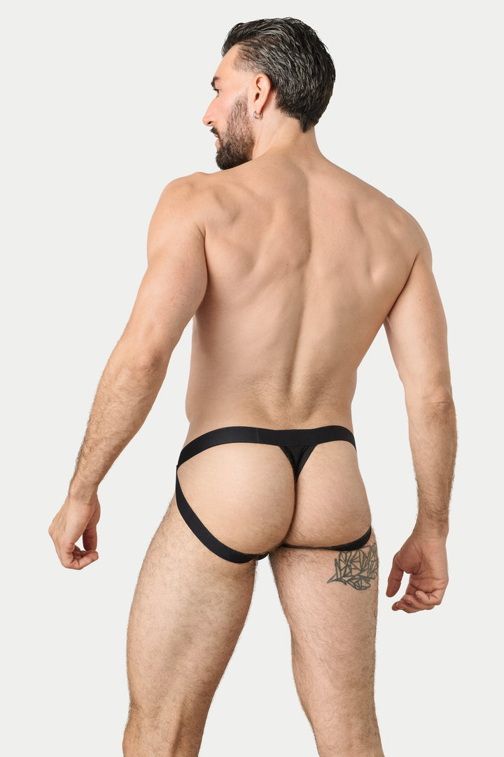 A muscular man shown from behind wearing a pair of black jockthong-style underwear, standing against a solid light gray background.