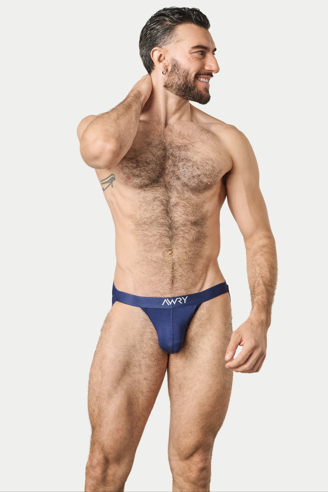 A muscular man modeling a dark blue jockstrap with a white 'AWRY' logo on the front, set against a solid light gray background.