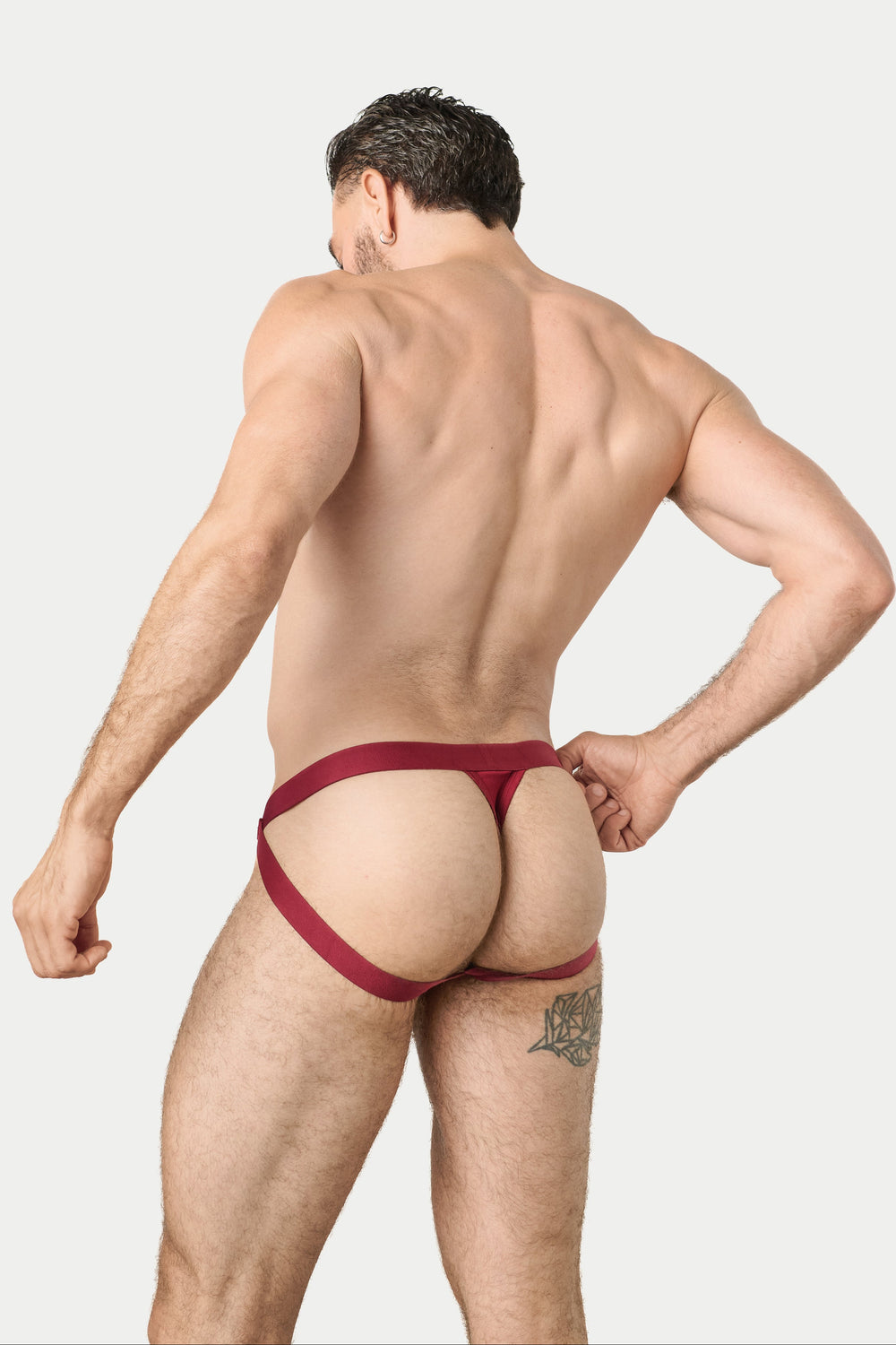 A muscular man shown from behind wearing a dark red jockthong-style brief, standing against a solid light gray background.