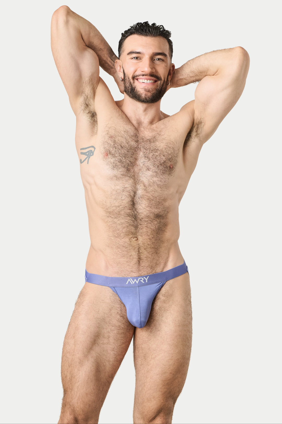 A muscular man posing in a light purple jockstrap with the brand name &