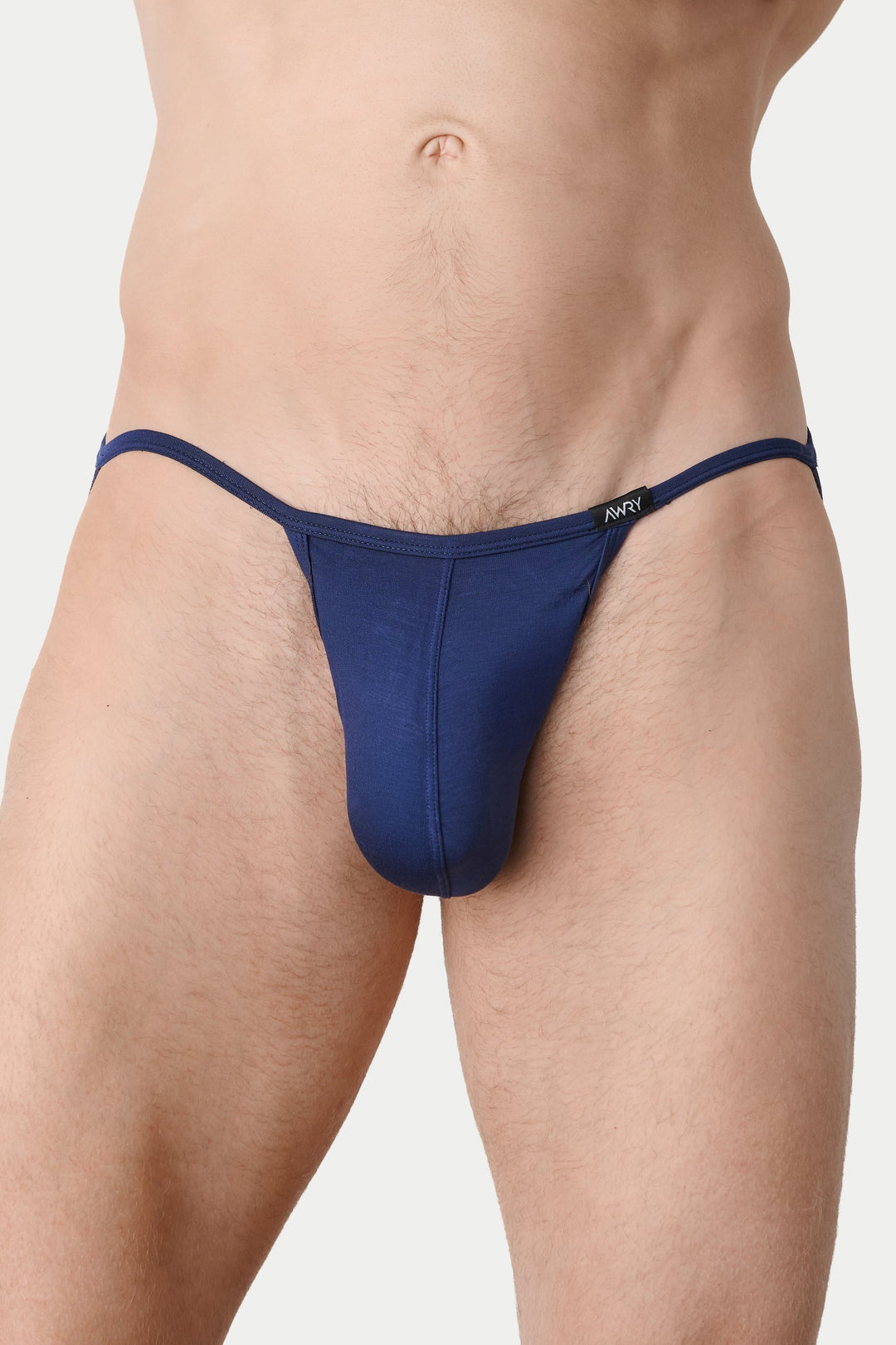 A close-up of a male model wearing a dark navy blue thong-style brief against a light gray studio background.