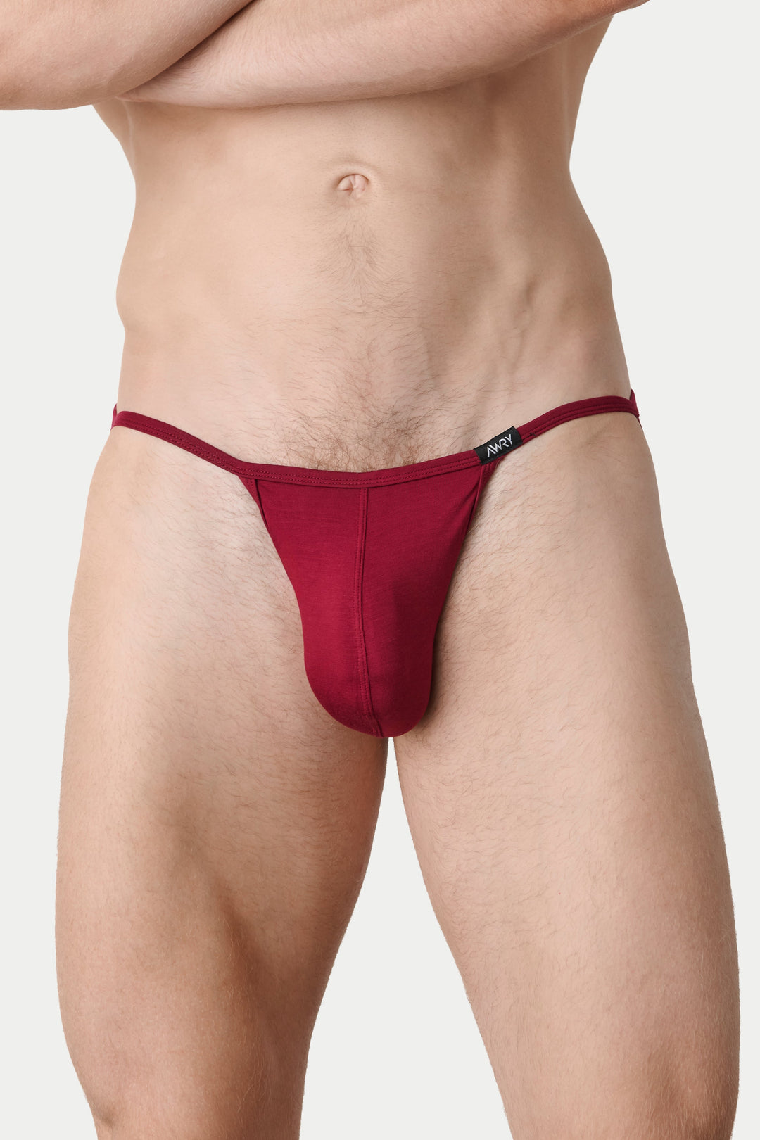 A close-up of a male model wearing a deep burgundy thong-style brief against a light gray studio background.
