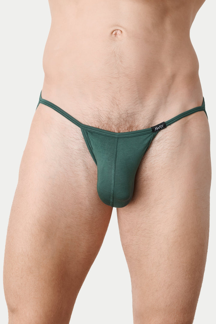 A close-up of a male model wearing a dark green thong-style brief against a light gray studio background.