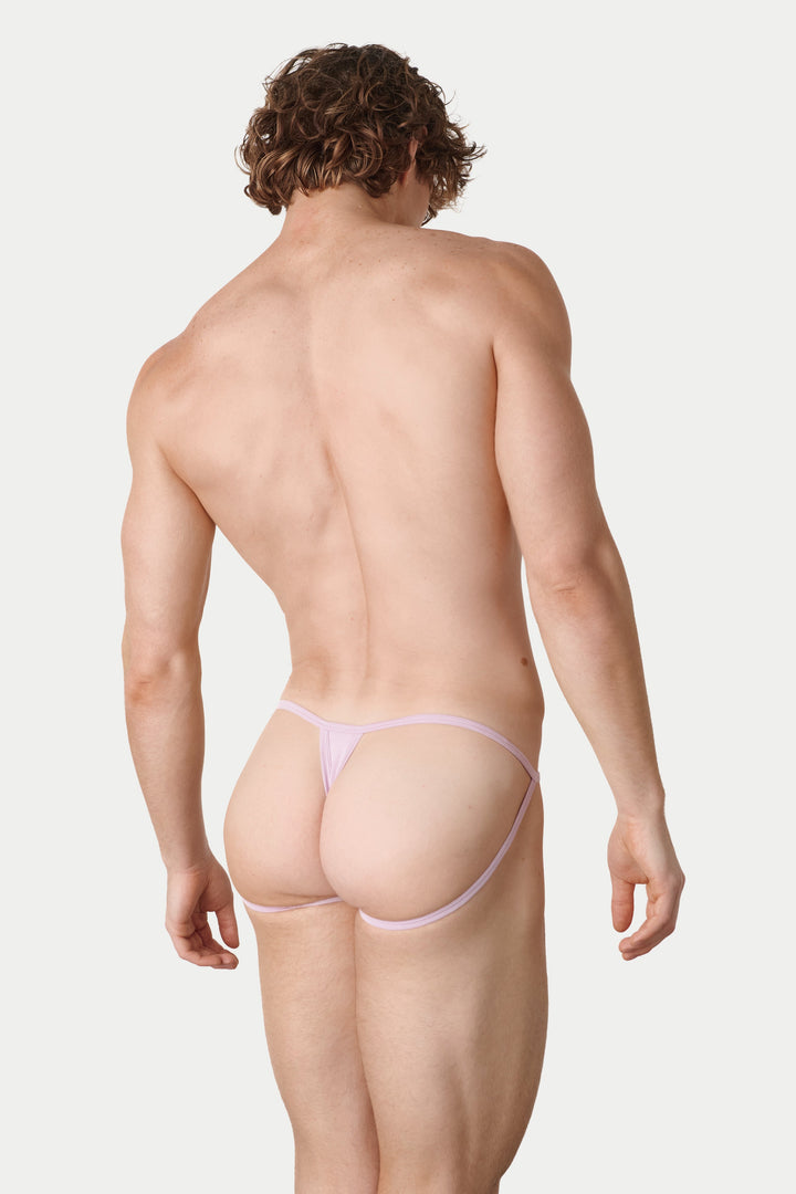 A man shown from the back wearing a very minimal light pink thong, photographed against a plain light gray studio background.
