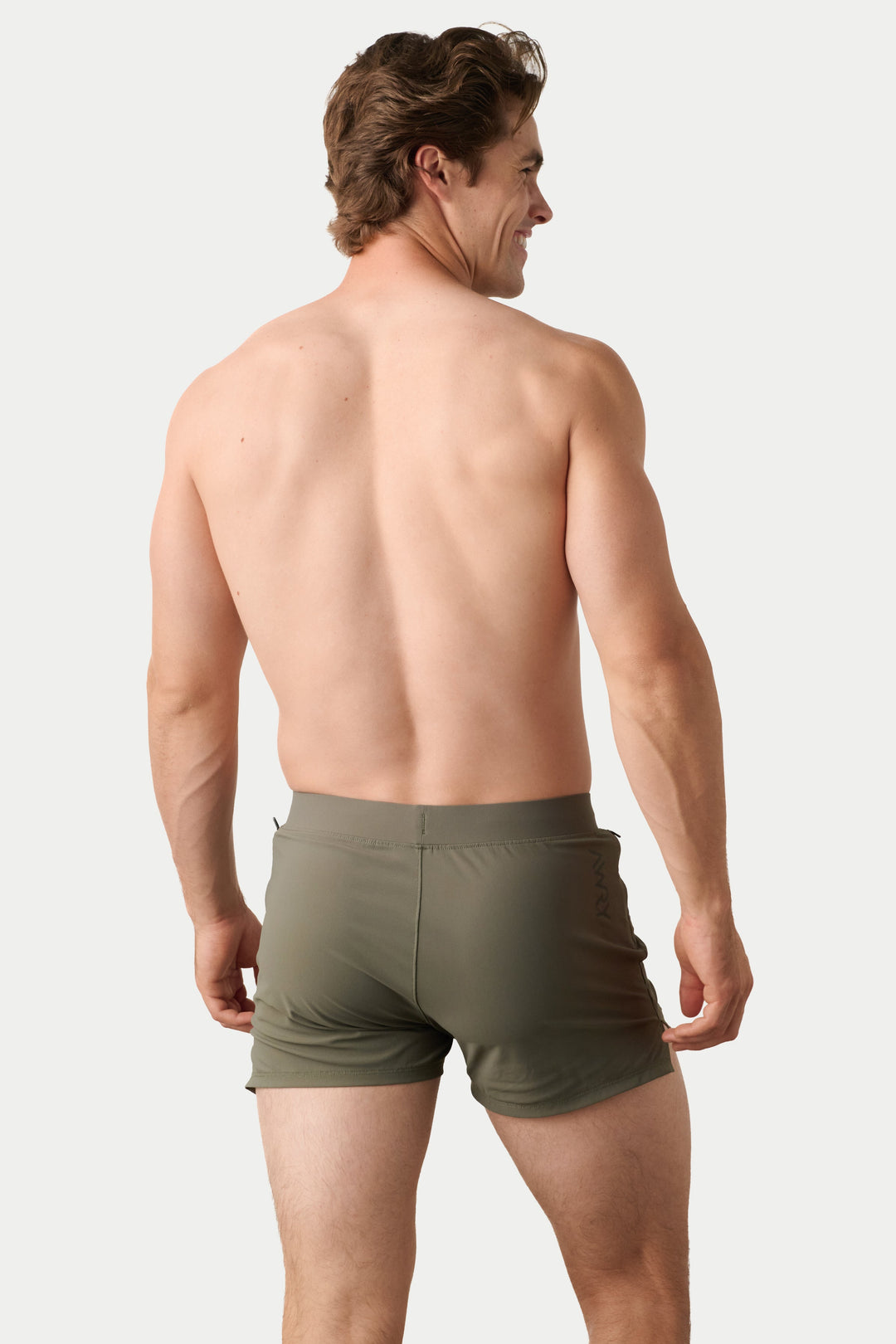 A man shown from the back wearing olive green athletic shorts against a light gray studio background.