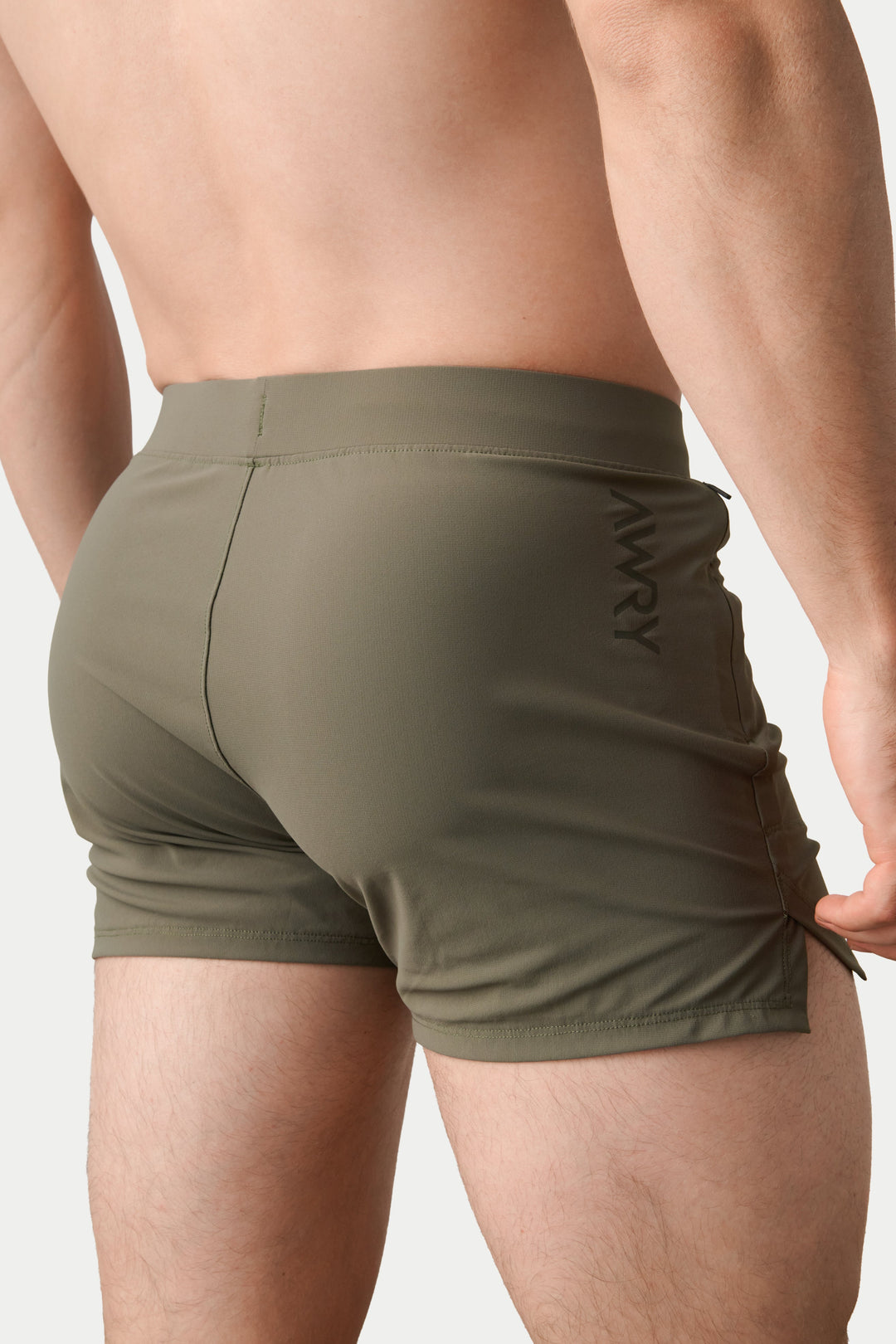 Rear view of a man wearing olive green athletic swim trunks with a drawstring side and a subtle vertical logo, set against a plain light gray background.