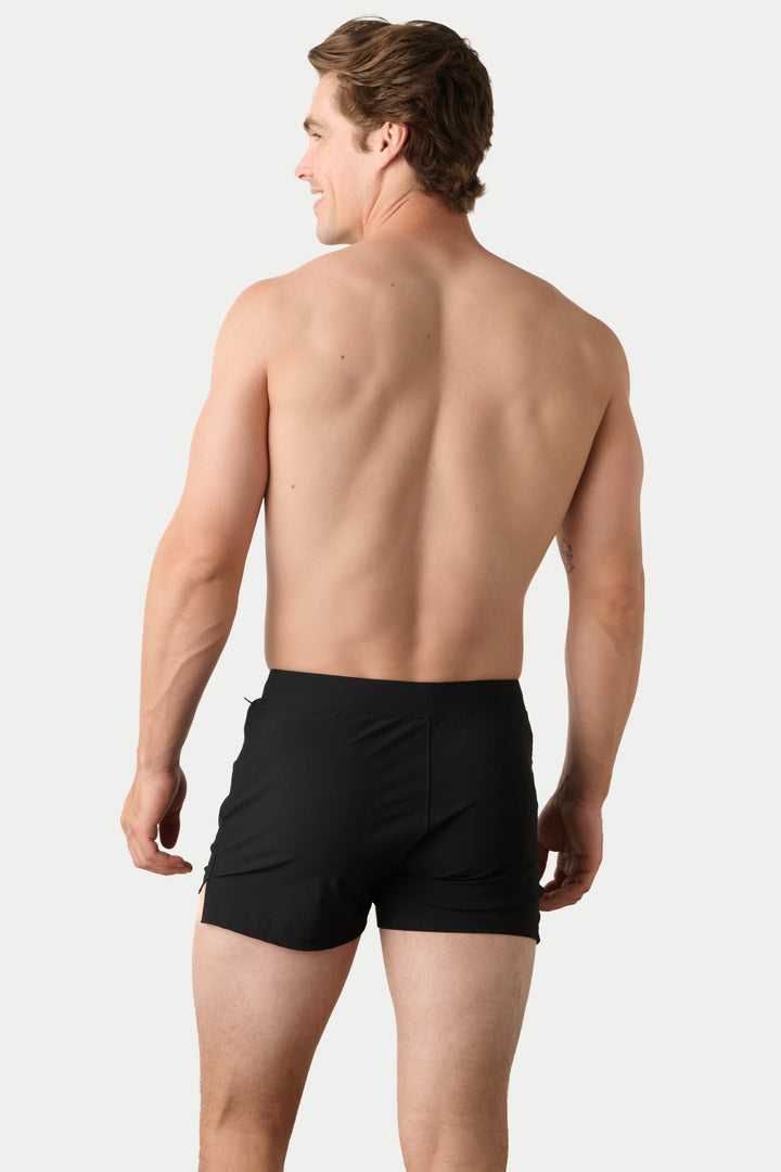 A man shown from the back wearing black swim trunks against a light gray studio background.
