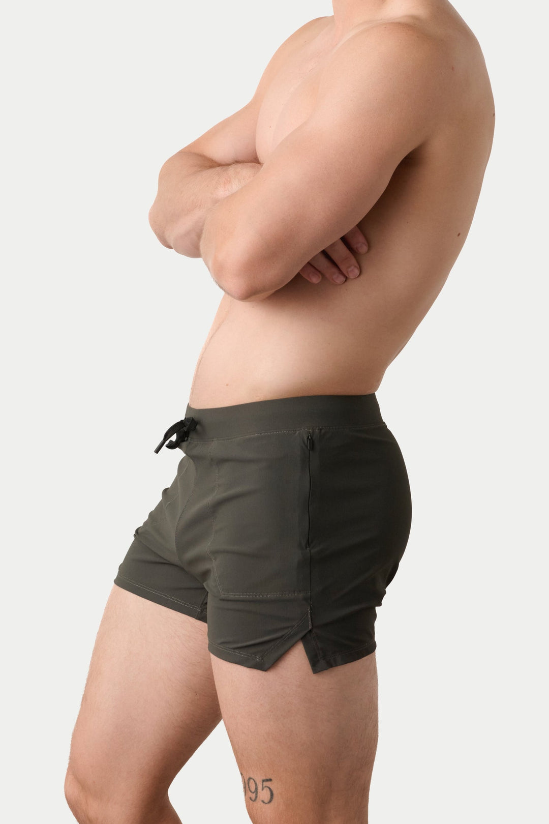 A man shown in side profile wearing dark gray athletic shorts, standing against a solid light gray background.