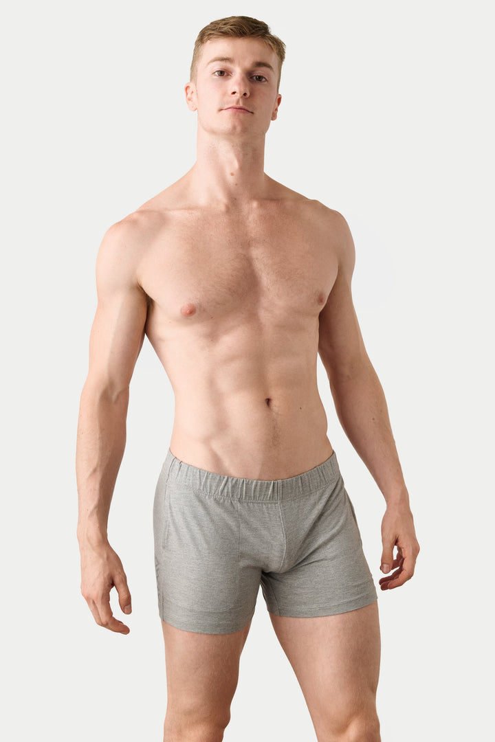 A shirtless male model wearing light gray boxer briefs, standing against a plain light gray studio background.