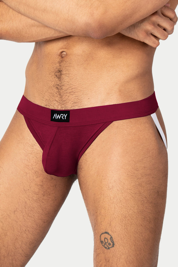 Berry red jockstrap with black waistband and AWRY brand label, shown on model from waist down.