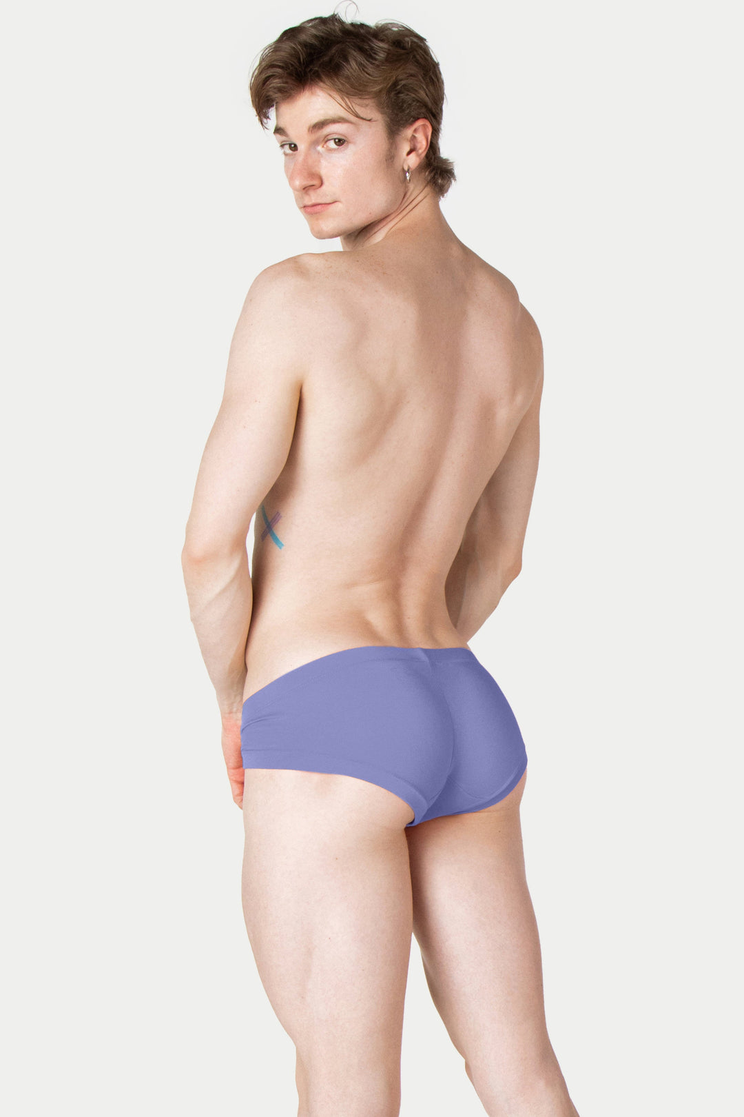 Person wearing lavender-gray VOGUE briefs with orange waistband trim, shown from behind.