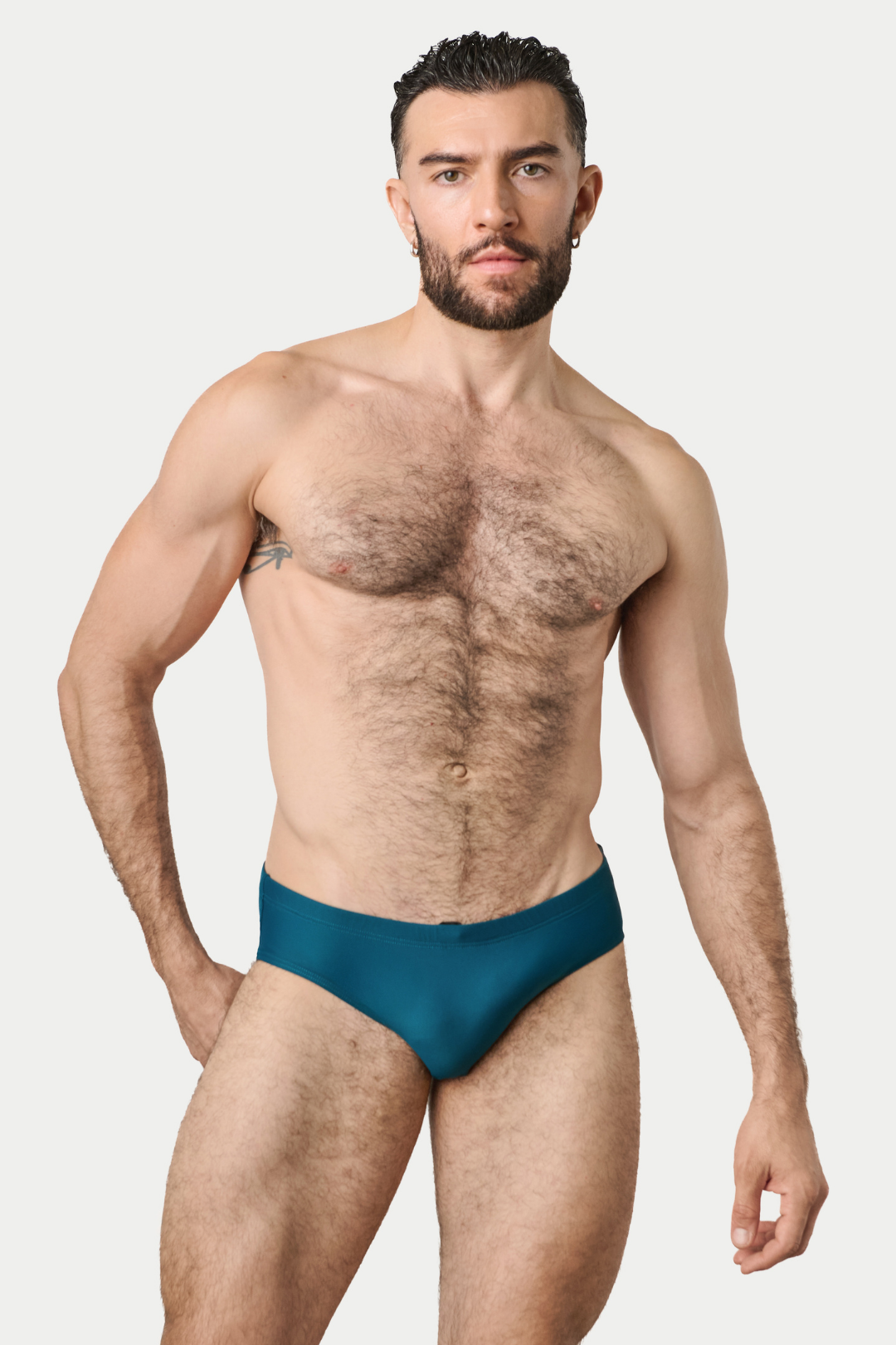 Man wearing teal swim brief with solid waistband and minimal coverage design.