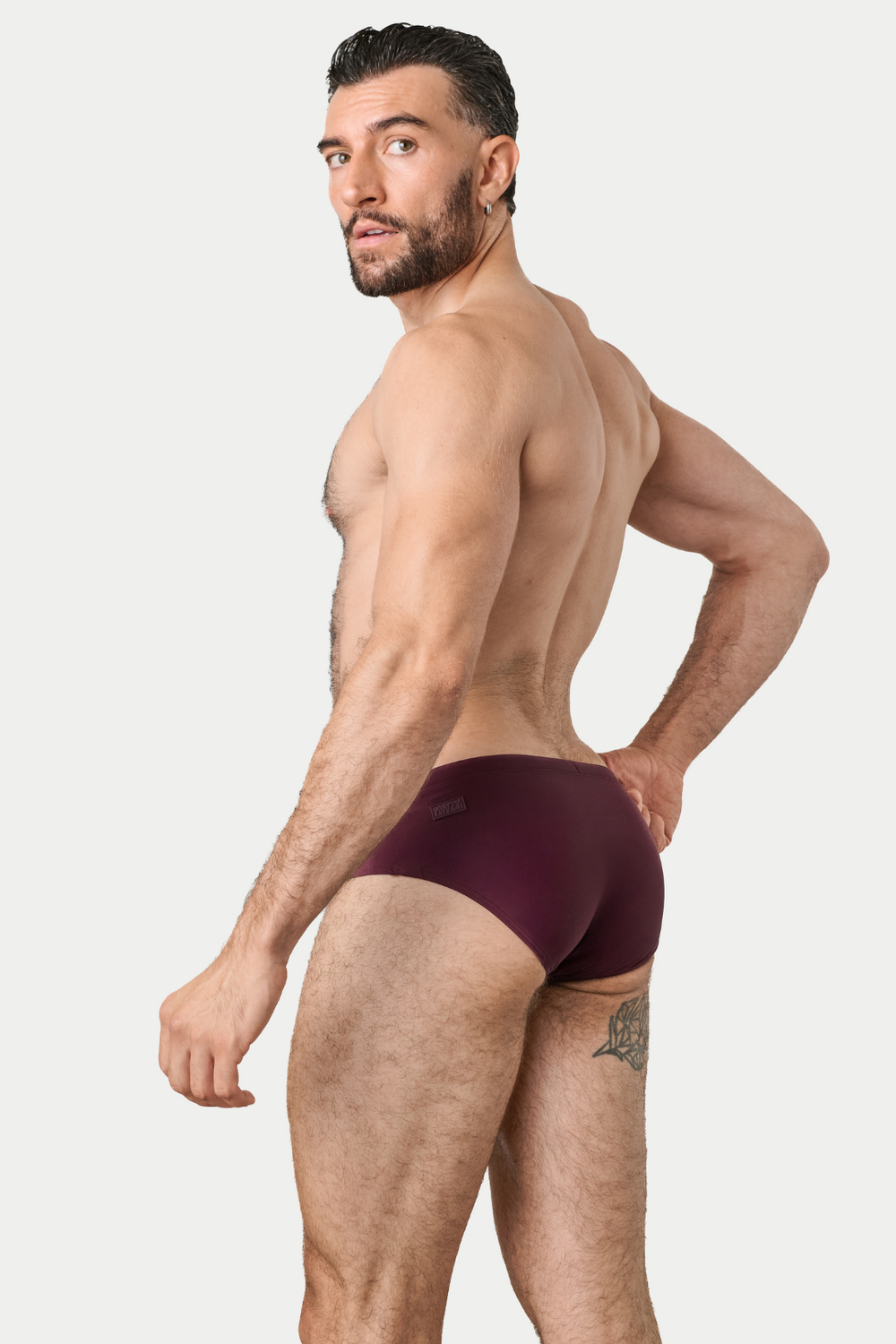 Man wearing burgundy swim brief with elasticated waistband, shown from side angle.