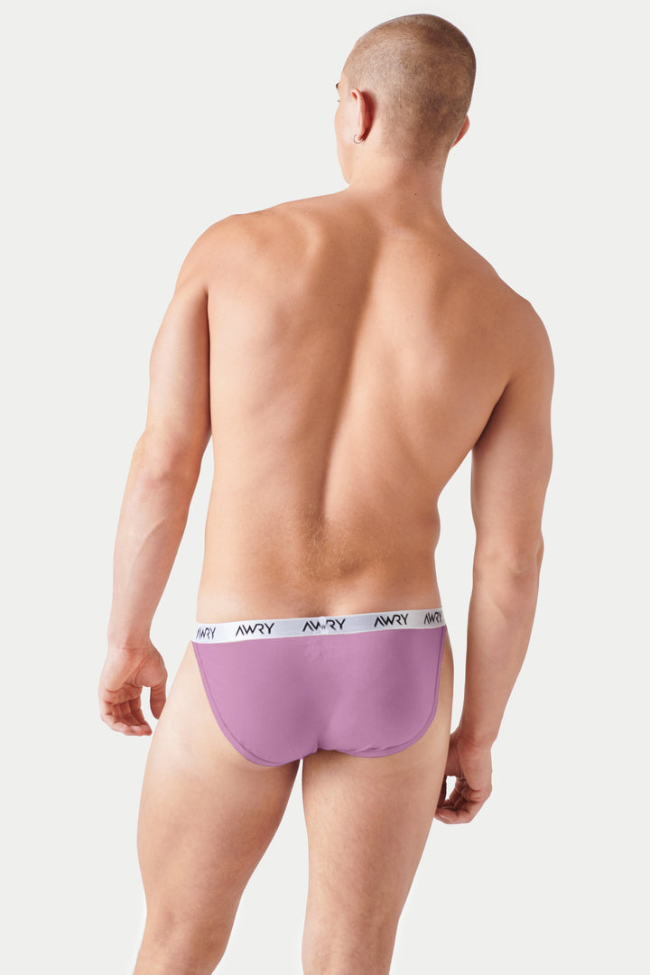 Pale pink tanga briefs with white waistband featuring AWRY branding, shown from back on male model.