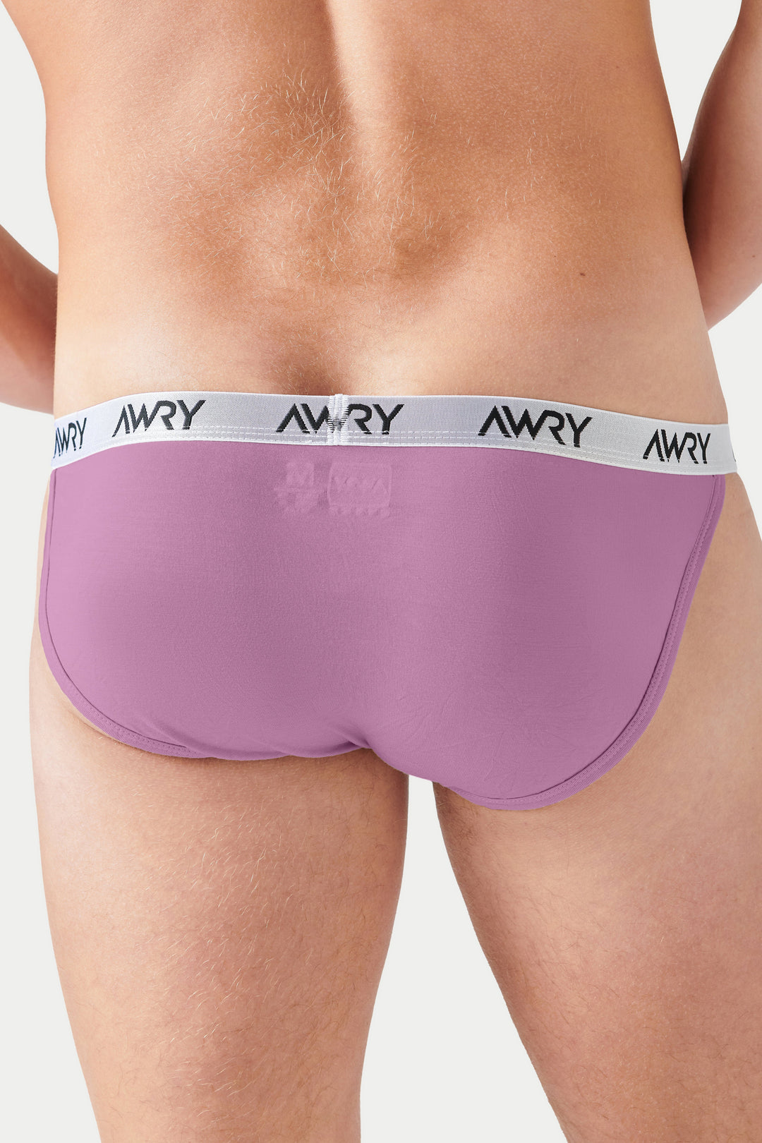 Pale pink tanga briefs with white waistband featuring "AWRY" text, shown on a model from waist down.
