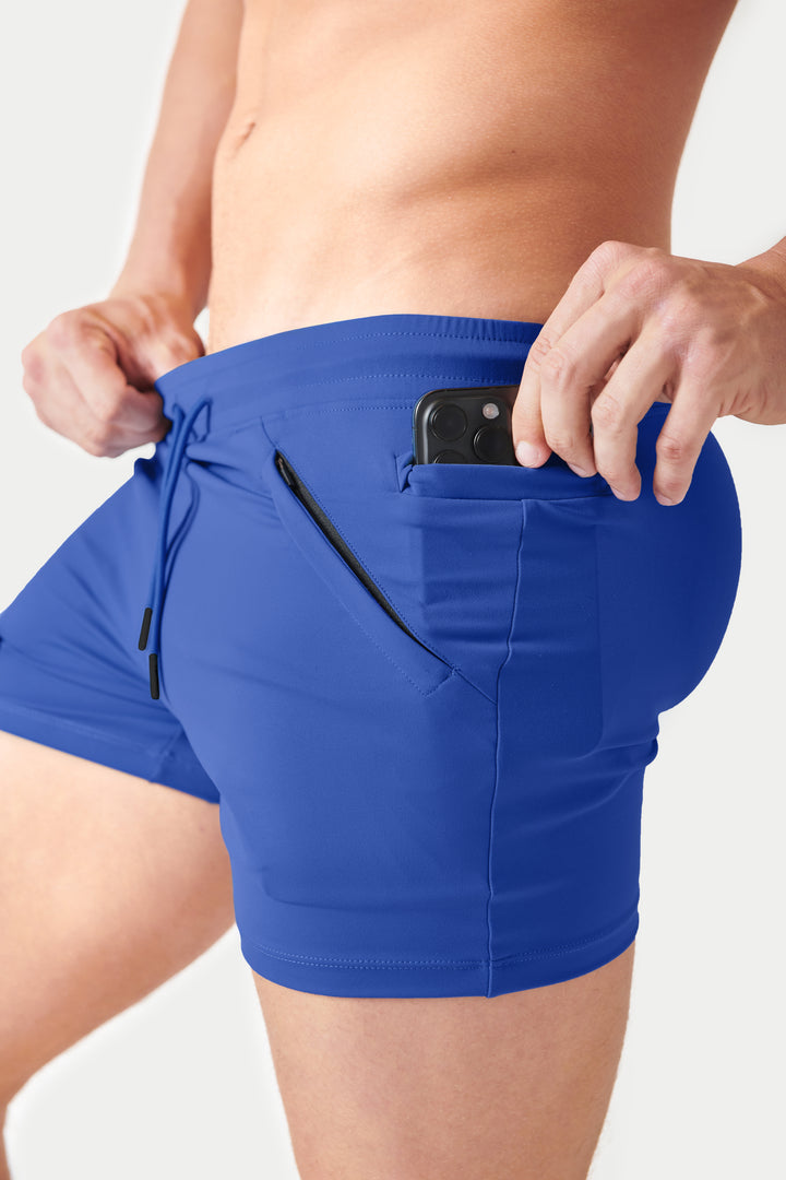 Cobalt blue shorts with drawstring waist, side pocket holding a phone, and black trim details.