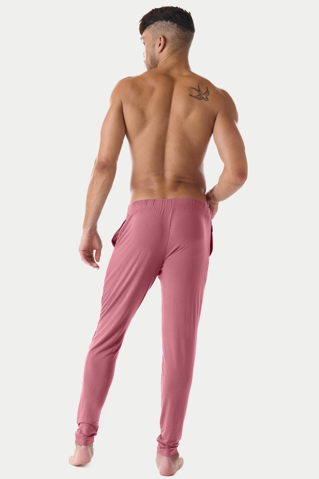 Man wearing blush pink lounge pants with elastic waistband and tapered ankles, shown from behind.