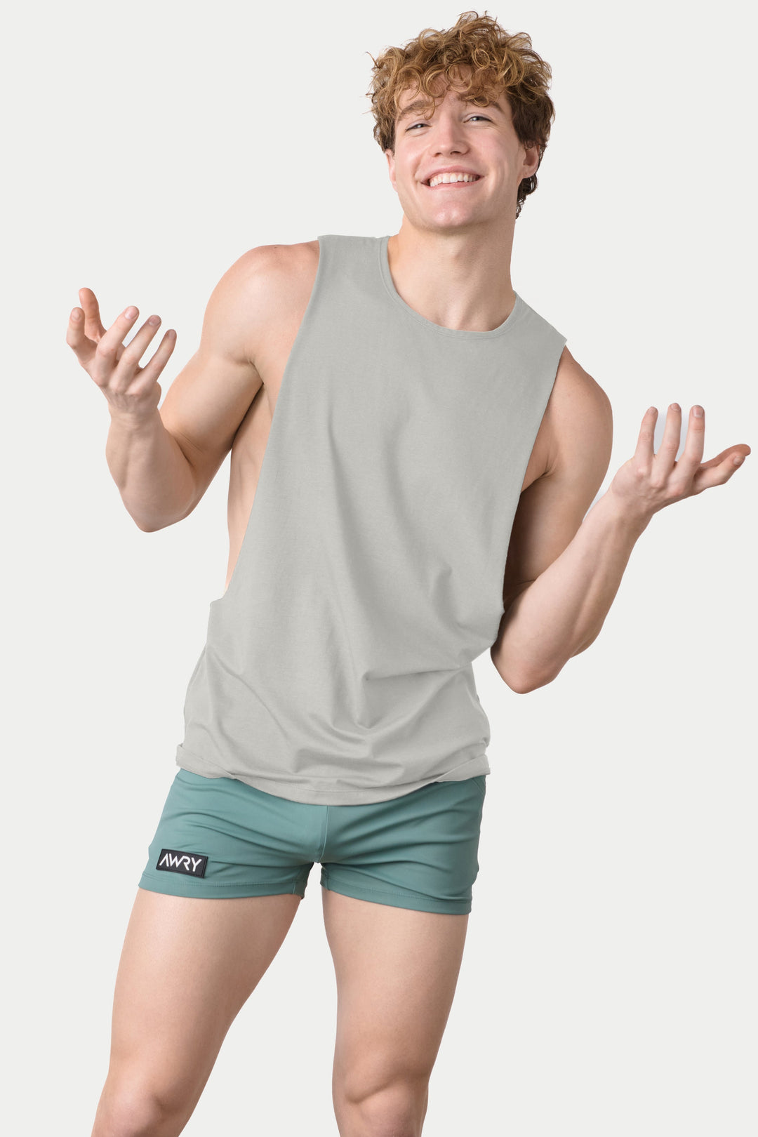 Man wearing stone-colored sleeveless tank top with teal shorts against white background.