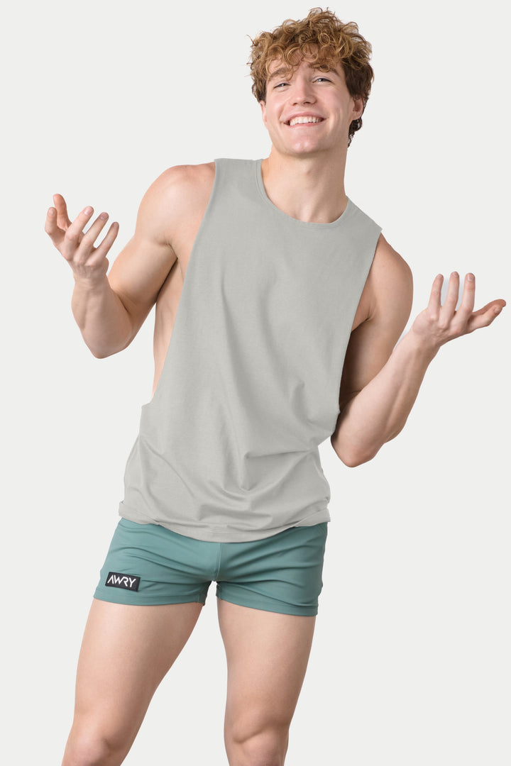 Man wearing stone-colored sleeveless tank top with teal shorts against white background.