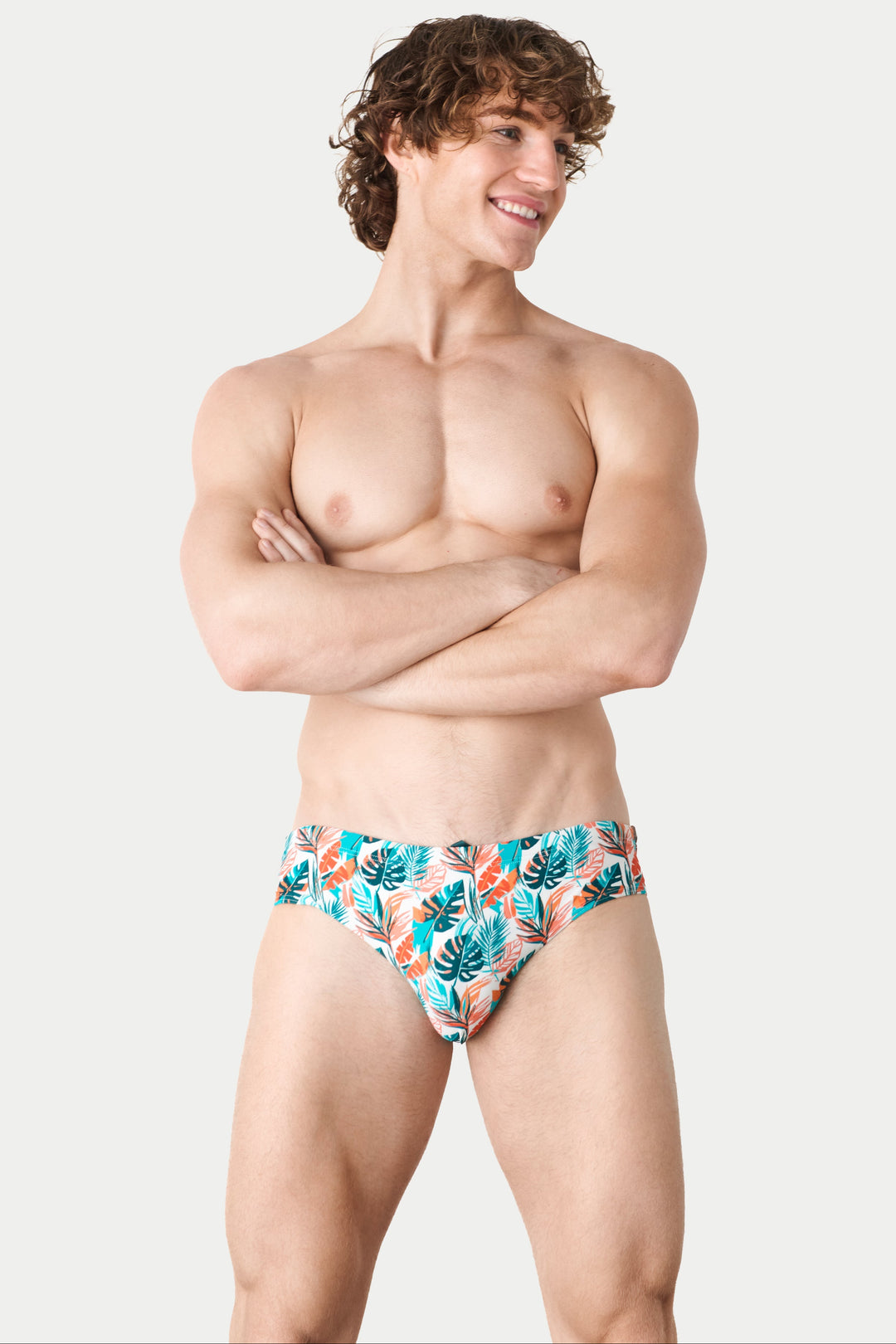 Man wearing tropical print swim brief with teal, orange, and white leaf pattern.