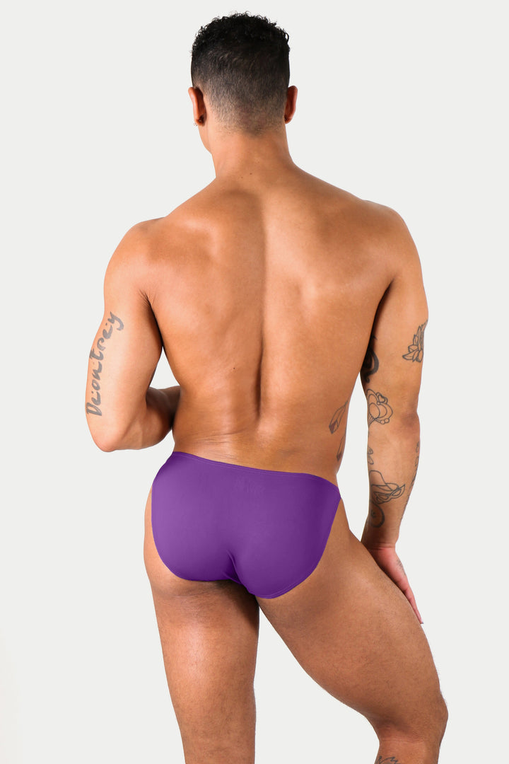 Man wearing purple bikini briefs, rear view against white background.